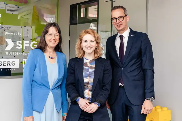 Zwei Frauen und ein Mann stehen vor einem Haus