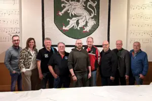 Neun Personen stehen vor einer Wand mit dem steirischen Wappen