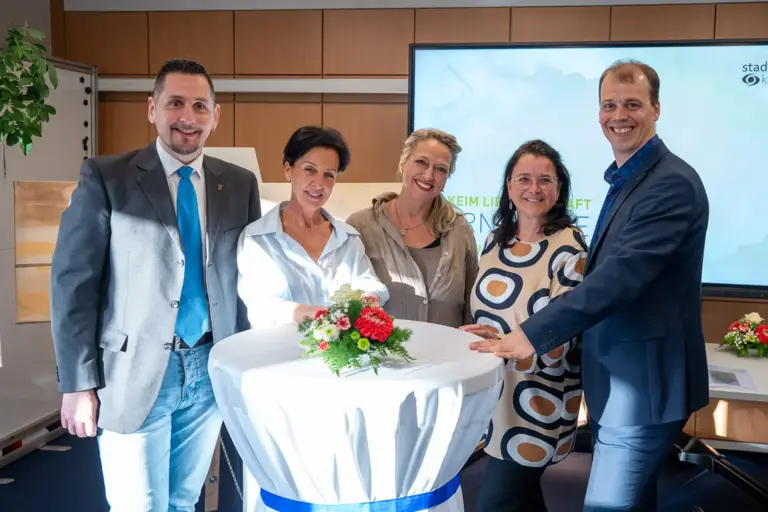 Zwei Männer und drei Frauen stehen an einem kleinen Tisch