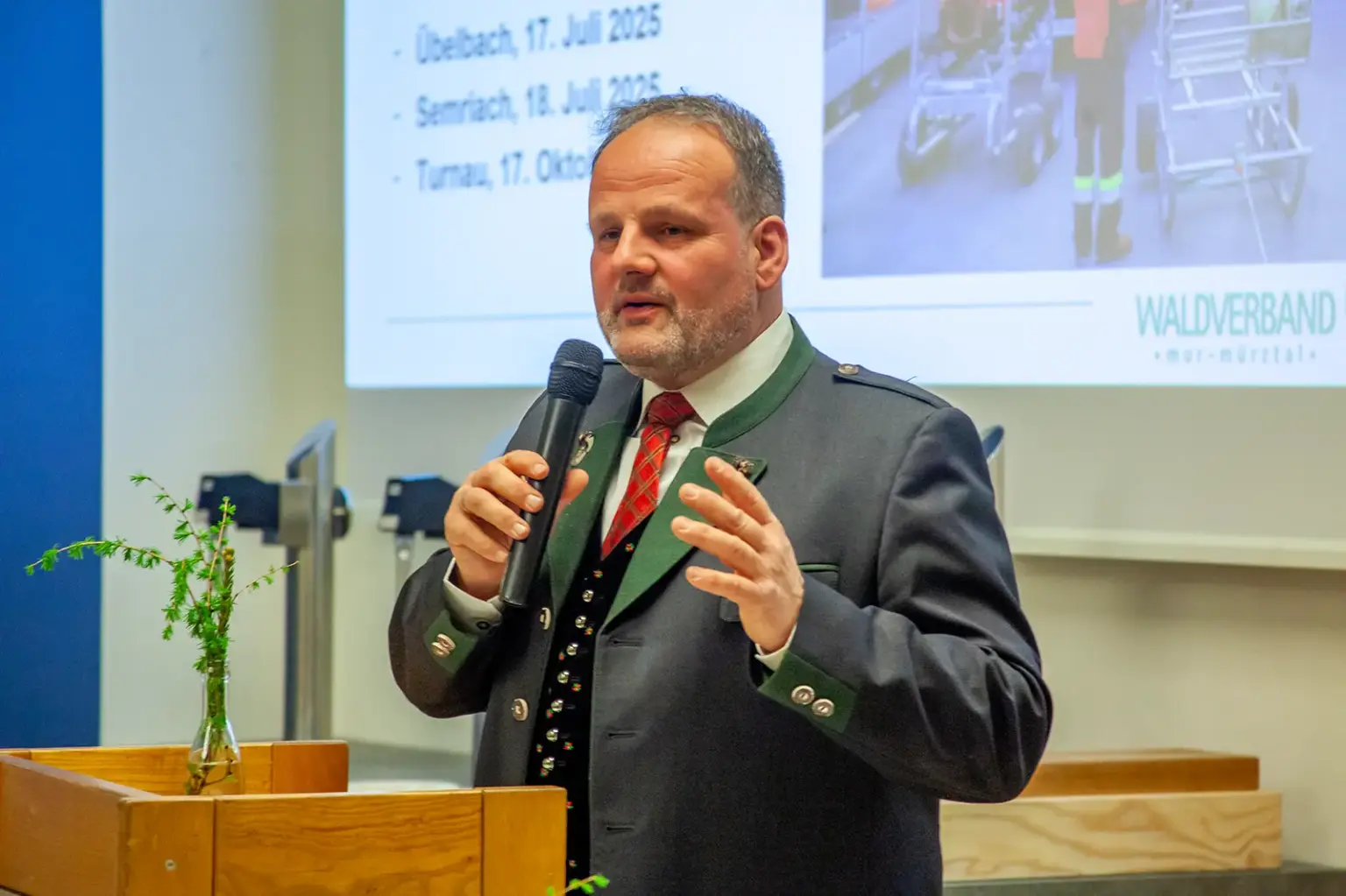Ein Mann im Steireranzug spricht an einem Rednerpult stehend in ein Handmikrofon