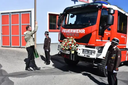 Zwei Männer in Uniform und ein Geistlicher stehen vor einem Feuerwehrauto