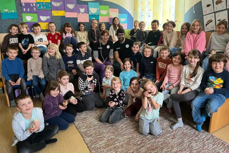 Eine große Gruppe von Kindern und zwei Erwachsene mit einigen Küken in einem grroßen Raum