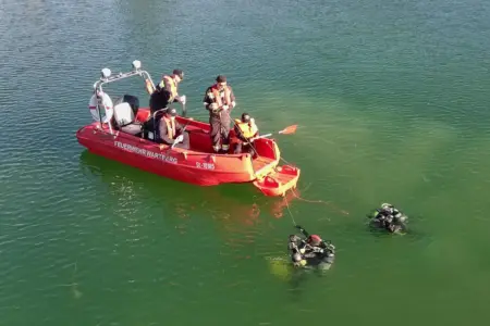 Einsatzkräfte der Feuerwehr in einem Rettungsboot. Zwei Rettungstaucher sind im Wasser.