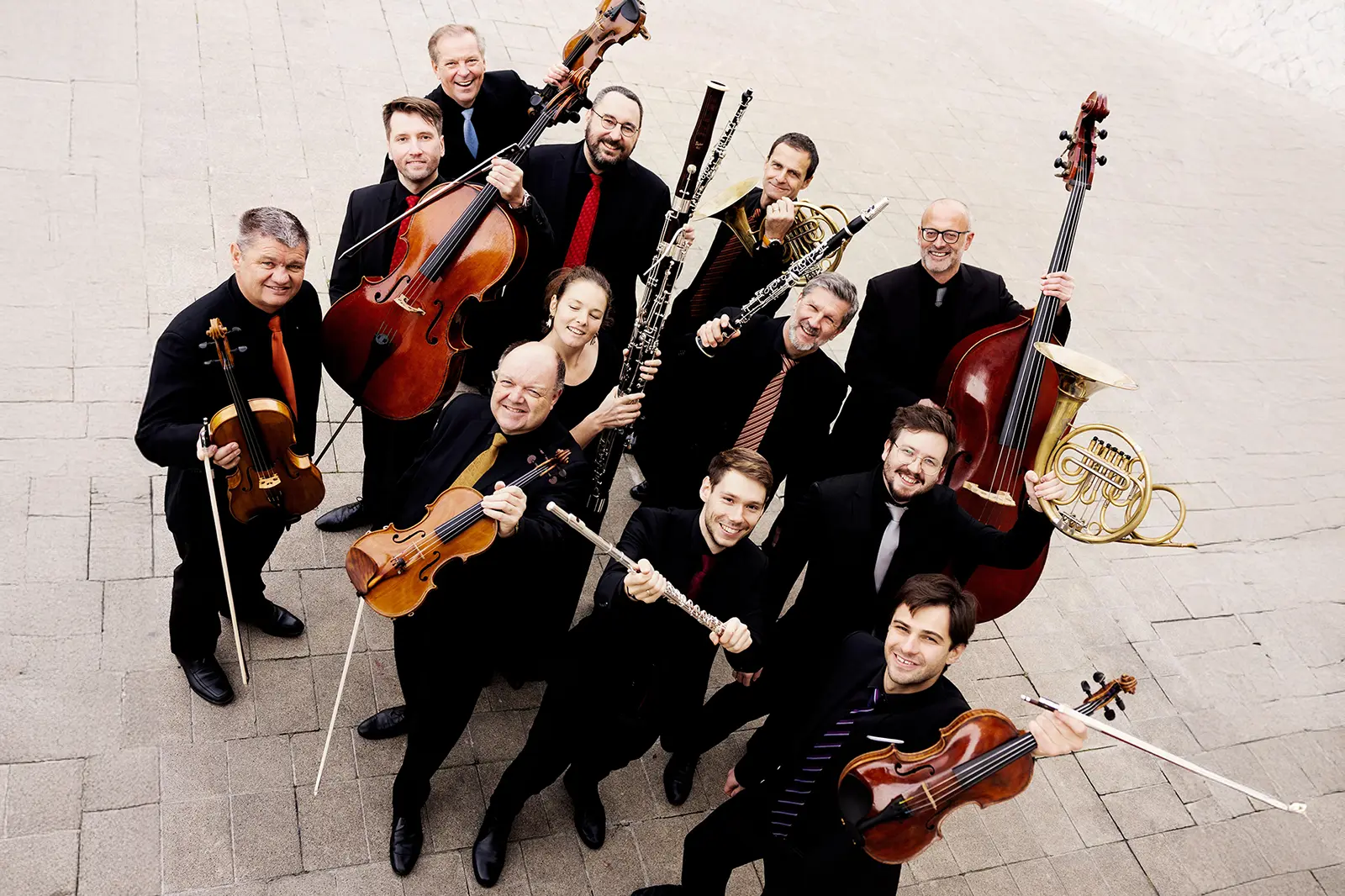 Eine Gruppe von Personen mit Musikinstrumenten steht auf einem gepflasterten Platz