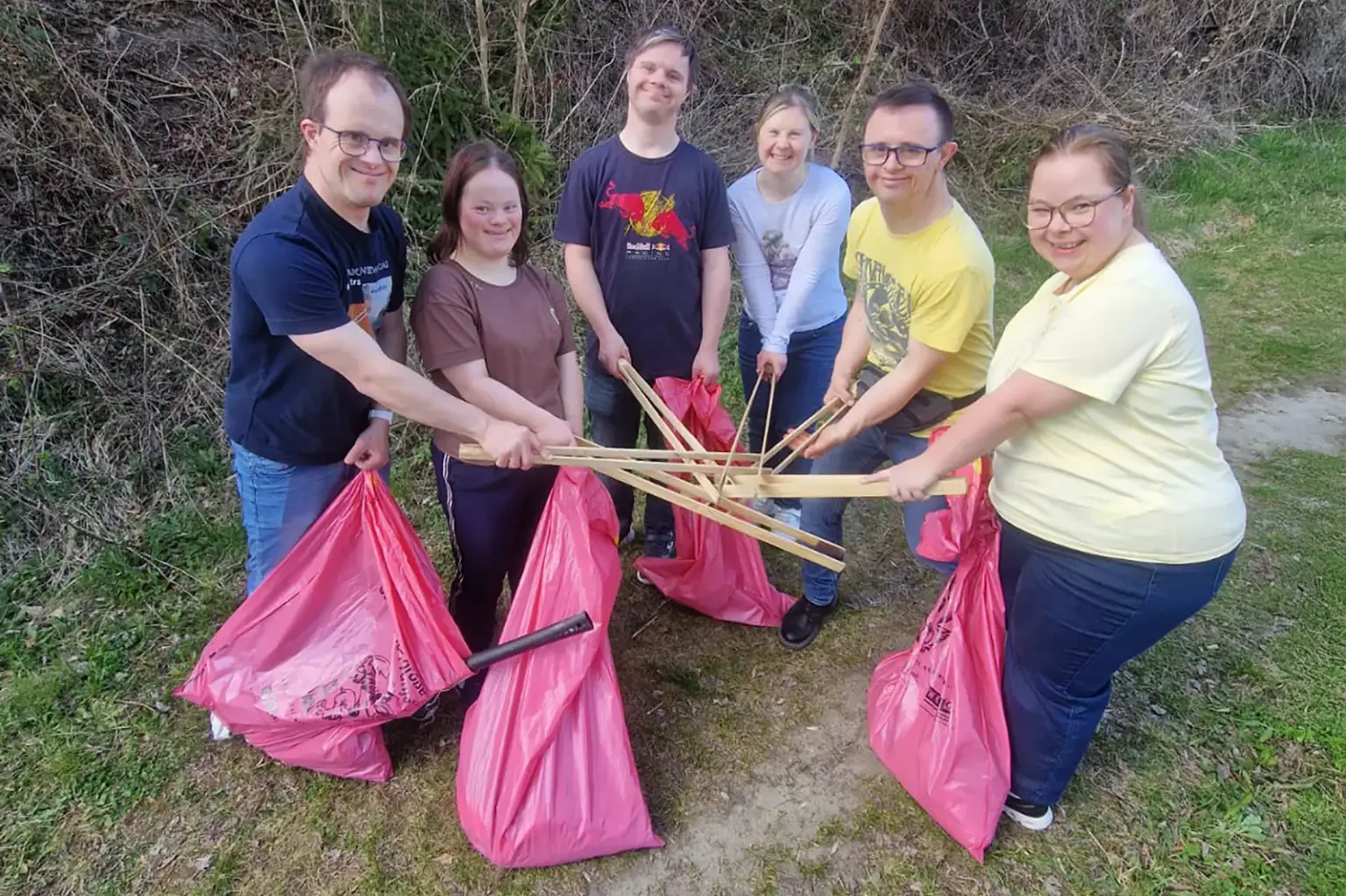Sechs Personen stehen mit Müllsäcken und Zangen auf einer Wiese