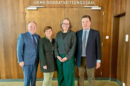 Zwei Frauen und zwei Männer in förmlicher Kleidung vor einer mit Holz vertäfelten Wand, über einer breiten zweiflügeligen Tür die Aufschrift "Gemeinderatssitzungssaal"