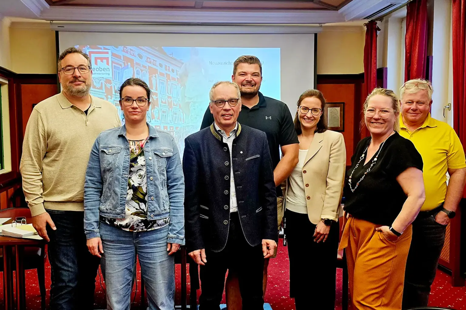 Vier Männer und drei Frauen stehen vor einer Leinwand