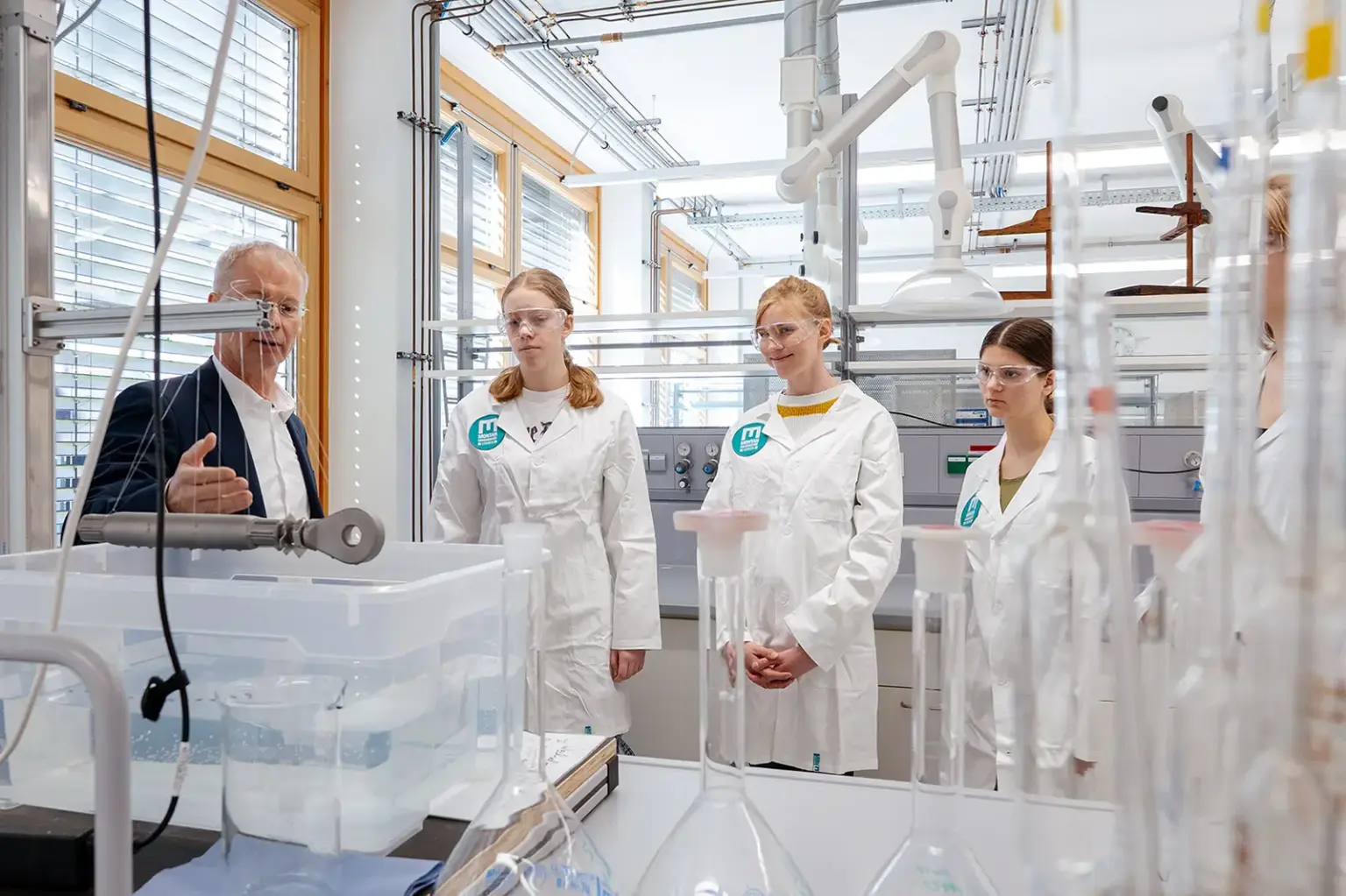 Vier Jugendliche in weißen Mänteln und ein älterer Erwachsener stehen an einem Labortisch