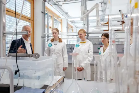 Vier Jugendliche in weißen Mänteln und ein älterer Erwachsener stehen an einem Labortisch