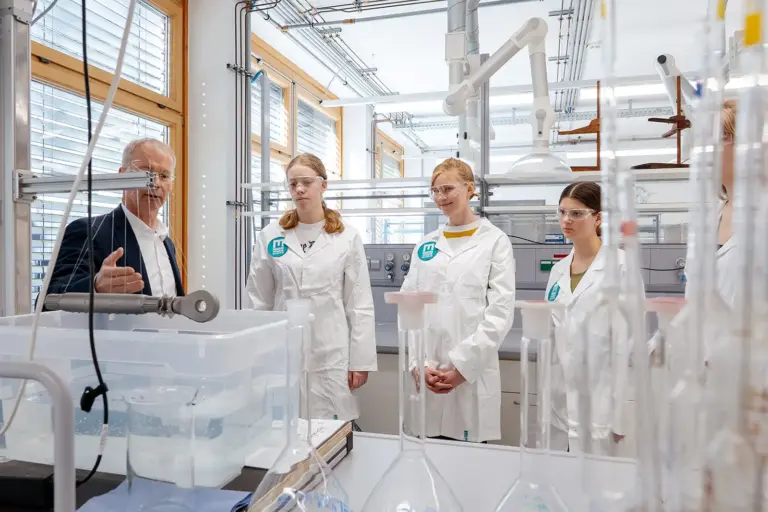 Vier Jugendliche in weißen Mänteln und ein älterer Erwachsener stehen an einem Labortisch