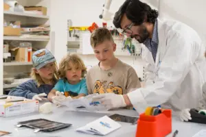 Drei Kinder und ein Erwachsener im weißen Mantel in einem Labor
