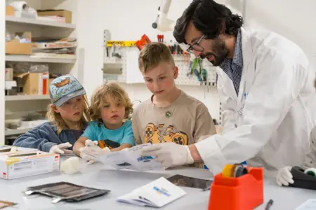Drei Kinder und ein Erwachsener im weißen Mantel in einem Labor