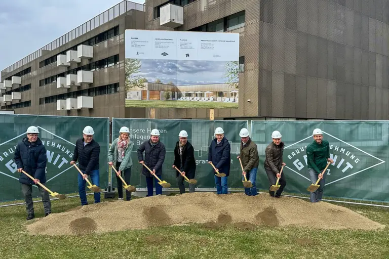Eine Gruppe von Personen mit Helmen und Schaufeln vor einer Schautafel