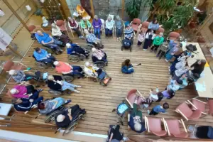 Eine Gruppe von älteren Personen, teils in Rollstühlen, mit Kindern in einem großen Raum