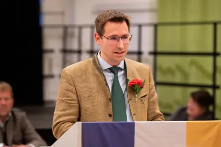 Ein Mann im Trachtenanzug mit Nelke am Revers steht an einem Rednerpult und spricht