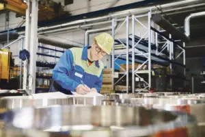 Ein Mann mit Helm macht Aufzeichnungen in einer Fabrikshalle