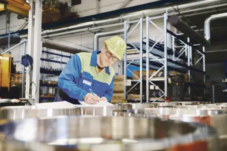 Ein Mann mit Helm macht Aufzeichnungen in einer Fabrikshalle