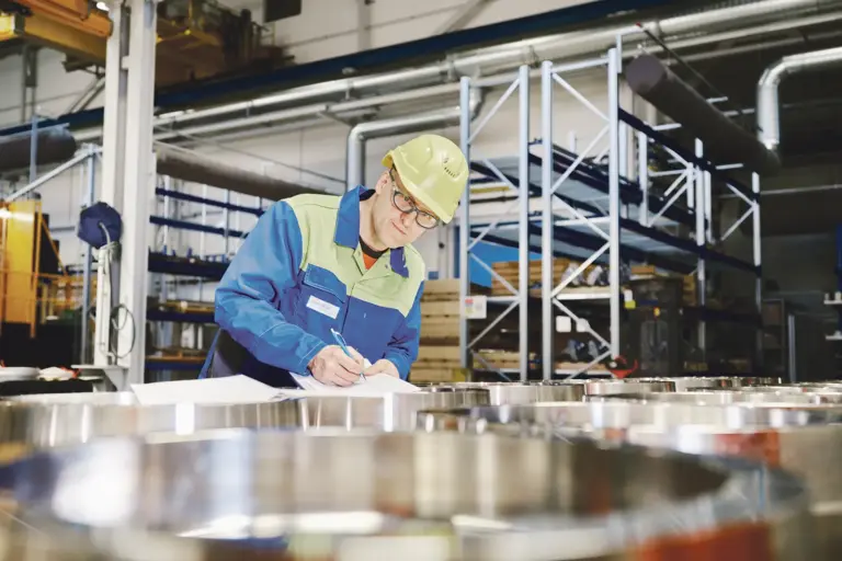 Ein Mann mit Helm macht Aufzeichnungen in einer Fabrikshalle