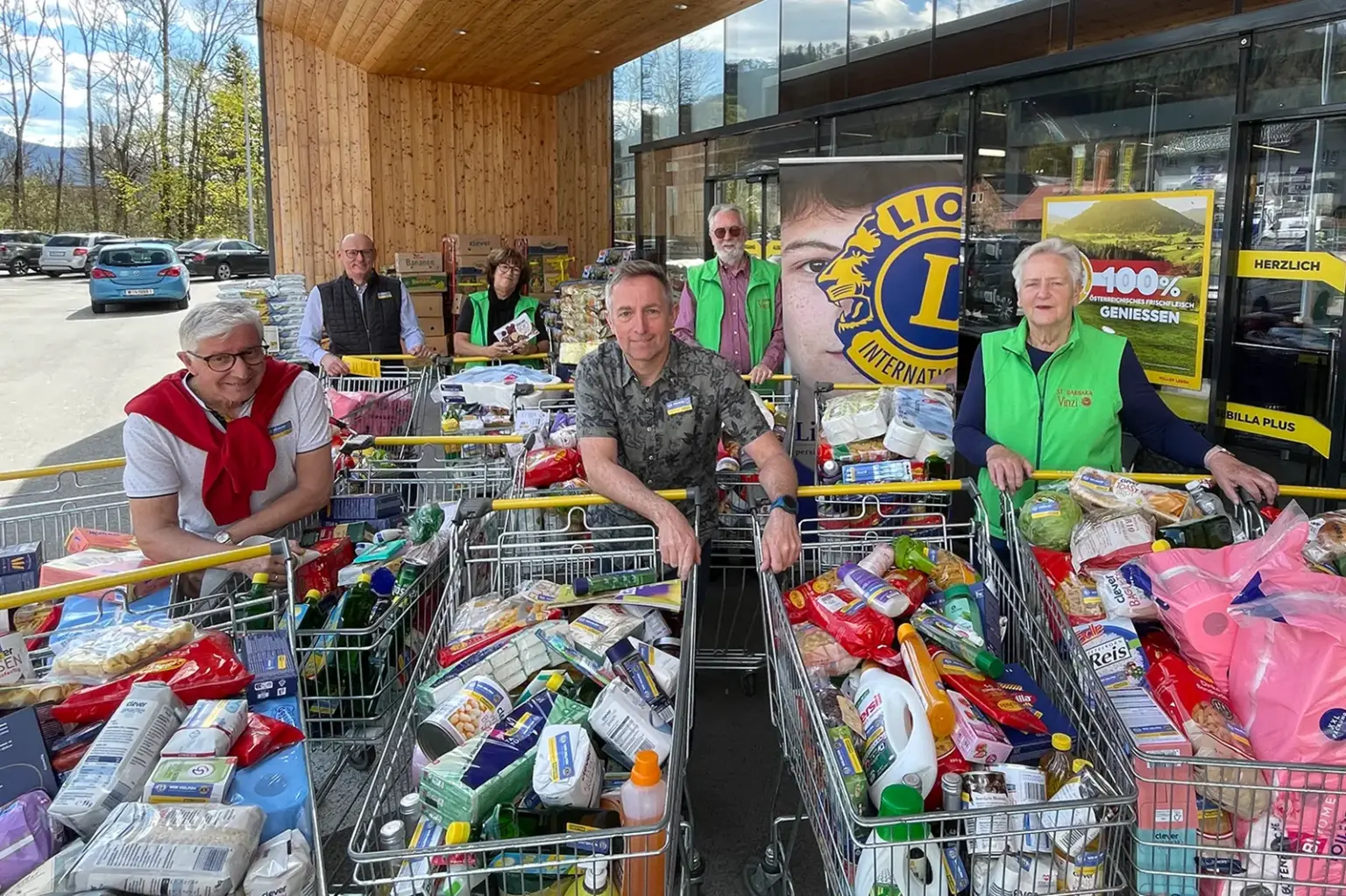 Sechs Personen stehen mit gefüllten Einkaufswagen vor einem Geschäft