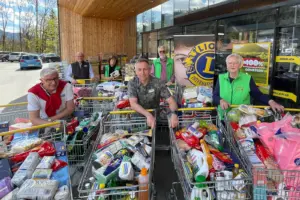 Sechs Personen stehen mit gefüllten Einkaufswagen vor einem Geschäft