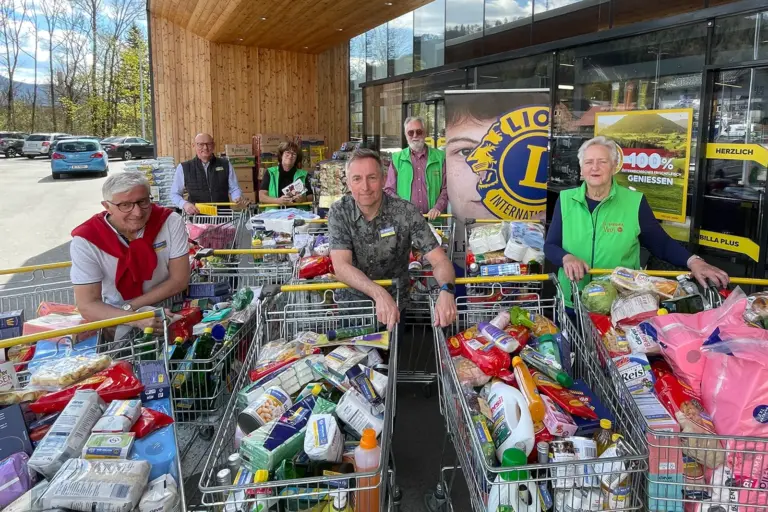 Sechs Personen stehen mit gefüllten Einkaufswagen vor einem Geschäft