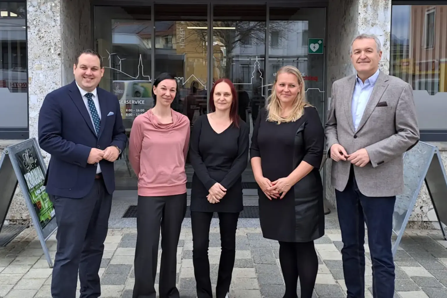 Zwei Männer und drei Frauen stehen vor einem Gebäude