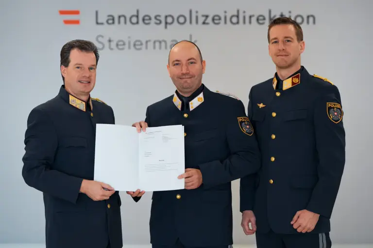 Drei Männer in Uniform zeigen eine Urkunde