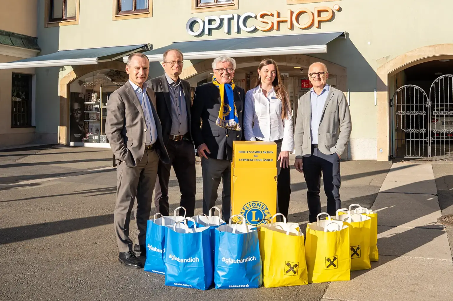 Vier Männer und eine Frau stehen mit vielen Papiersäcken auf einem Platz