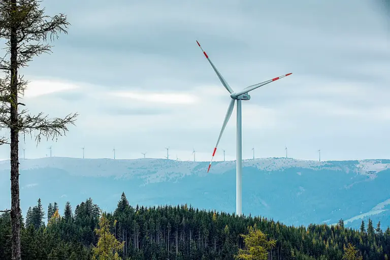 Eine Windkraftanlage auf einem bewaldeten Berg, im Hintergrund in höhergelegenen Almgelände mehr als zehn weitere Windräder