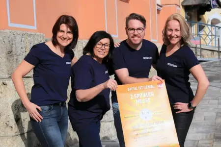 Drei Frauen und ein Mann halten gemeinsam ein Plakat.