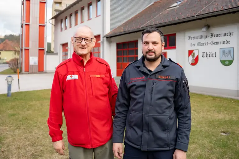 Zwei Männer in Uniform stehen vor einem Feuerwehrhaus