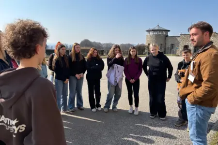 Eine Gruppe Jugendlicher steht auf einem großen Platz vor einer Mauer mit einem Turm