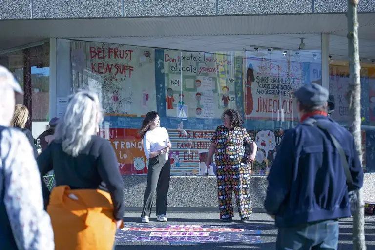 Zwei Frauen und mehrere Zuschauer stehen vor einem Schaufenster voller Spruchbänder