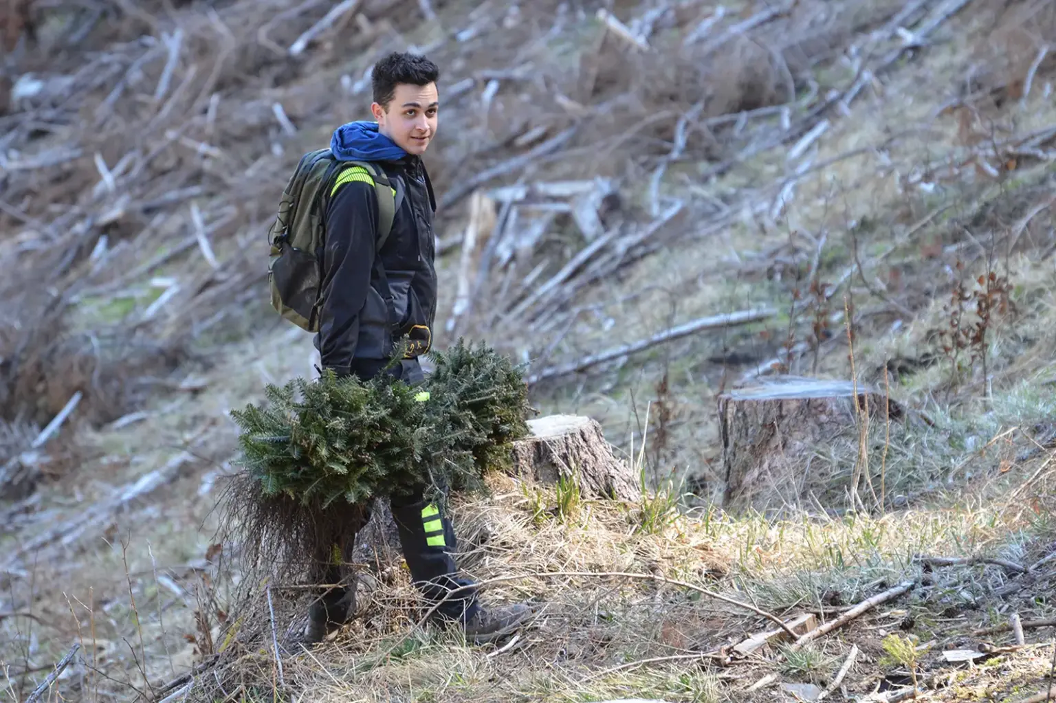Ein jugendlicher steht mit einem jungen Baumschößling an einem Hang