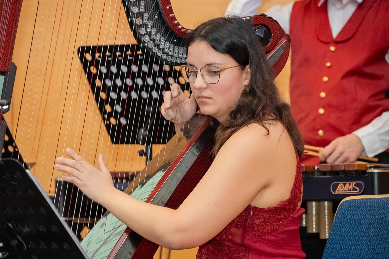Eine Frau mit rotem Kleid und Brille spielt eine Harfe
