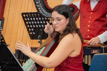 Eine Frau mit rotem Kleid und Brille spielt eine Harfe