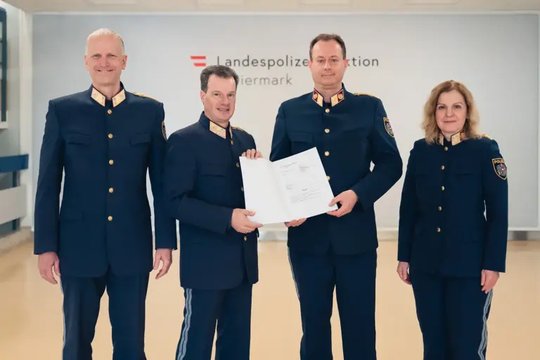 Drei Männer und eine Frau in Uniform halten eine Urkunde