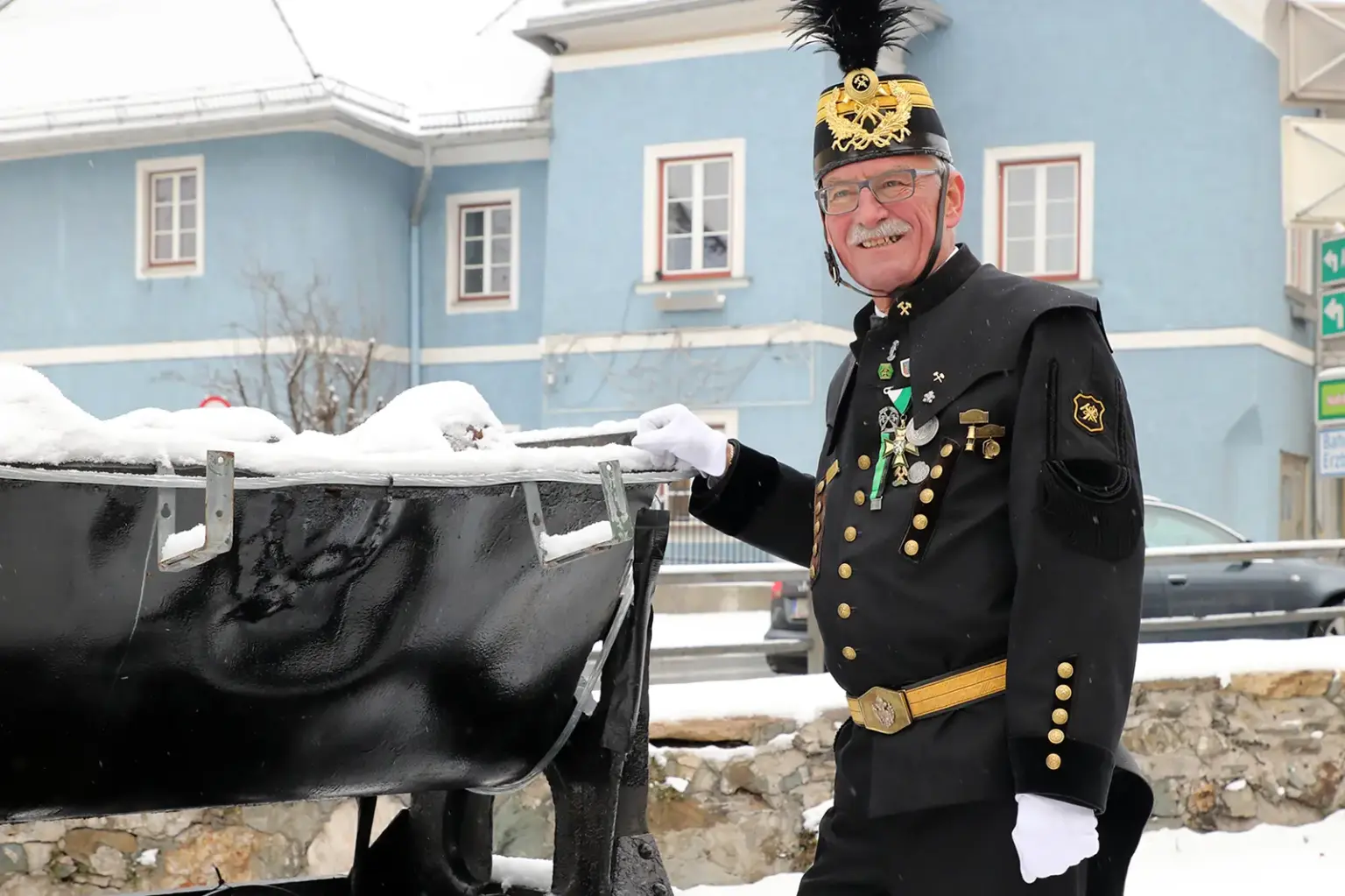 Ein älterer Mann in Bergmannskittel lehnt an einem Grubenhunt