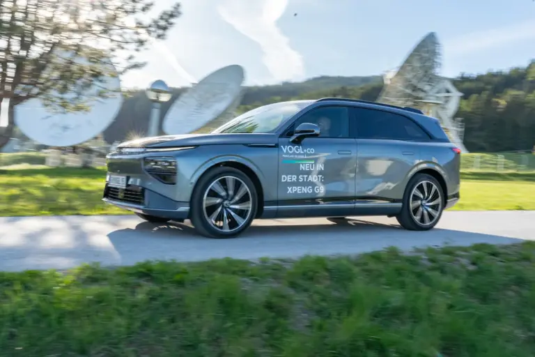Ein Auto der Karosserieform SUV fährt auf einer Landstraße von rechts nach links, im Hintergrund drei große Parabolantennen