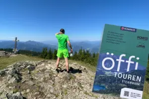 Ein Mann steht auf einem Berggipfel und schaut in die Ferne. Im rechten Bilddrittel die Umschlagseite eines Wanderbuchs.