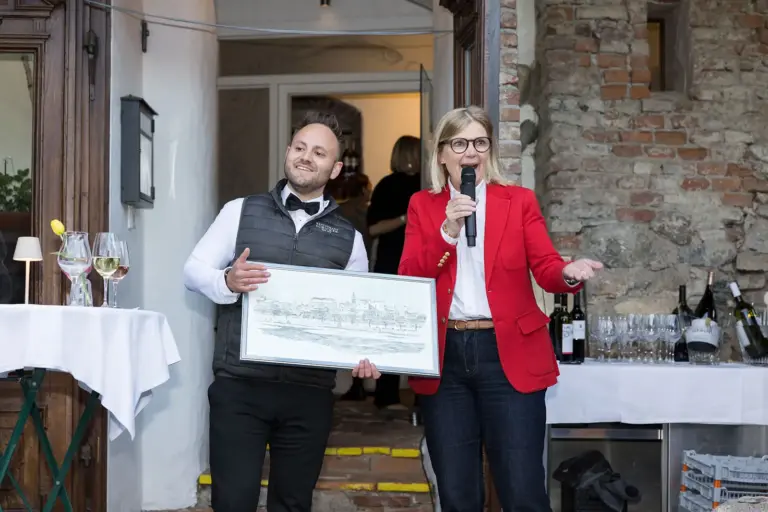 Restaurant Schicker im Brucker Baderhaus eröffnet Ein Mann mit gerahmtem Bild und eine Frau mit Mikrofon in Händen, beide lachend