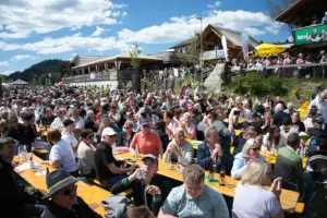 Ein Freiluft-Festgelände mit zahlreichen an Biertischen sitzenden Gästen