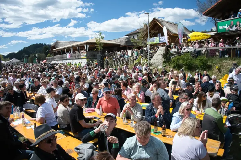 Ein Freiluft-Festgelände mit zahlreichen an Biertischen sitzenden Gästen