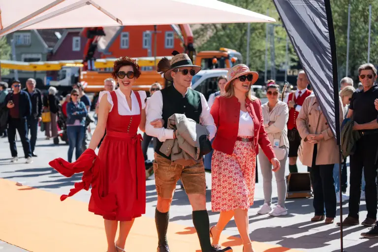 Zwei Frauen und ein Mann in Tracht gehen bei einer Freiluft-Modenschau über einen roten Teppich
