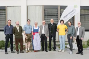 Eine Frau und acht Männer vor einem Gebäude und einer Fahne mit Logo des Alpenvereins.
