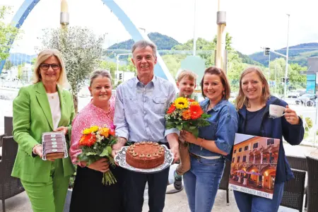 Vier Frauen, ein Mann und ein Kind halten Blumen und Mehlspeisen