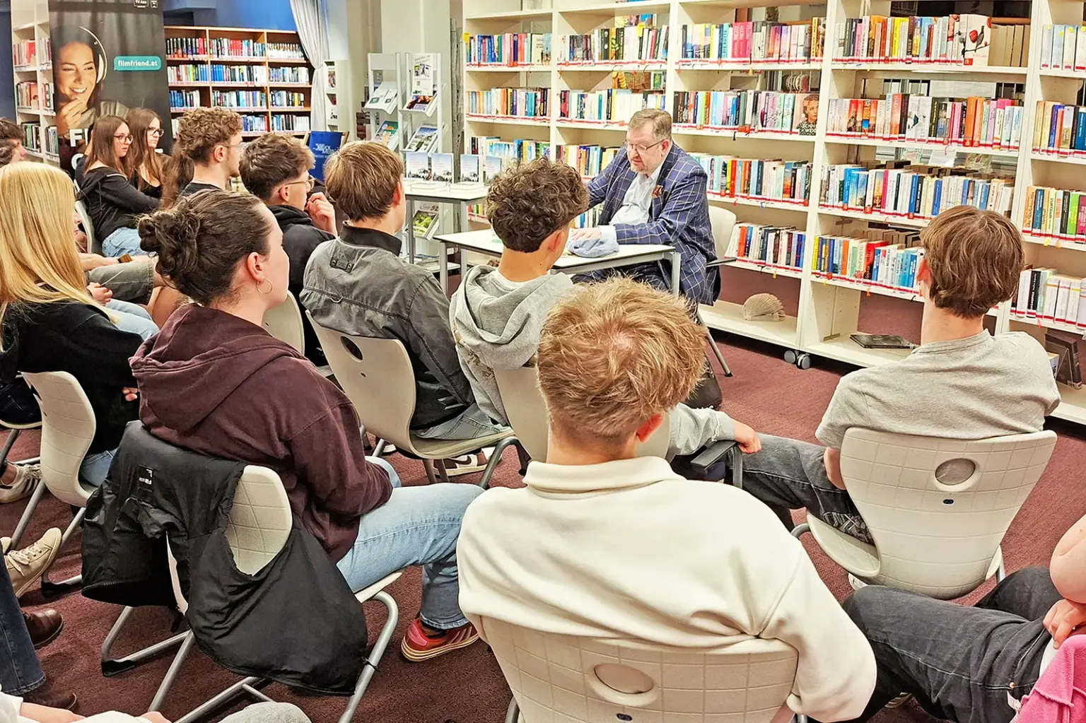 Lesung in der Stadtbücherei Bruck Ein Mann liest in einer Bibliothek vor Jugendlichen aus einem Buch