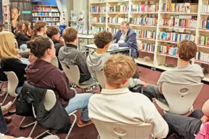 Ein Mann liest in einer Bibliothek vor Jugendlichen aus einem Buch