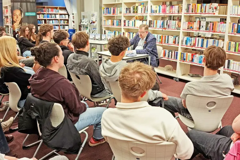 Lesung in der Stadtbücherei Bruck Ein Mann liest in einer Bibliothek vor Jugendlichen aus einem Buch