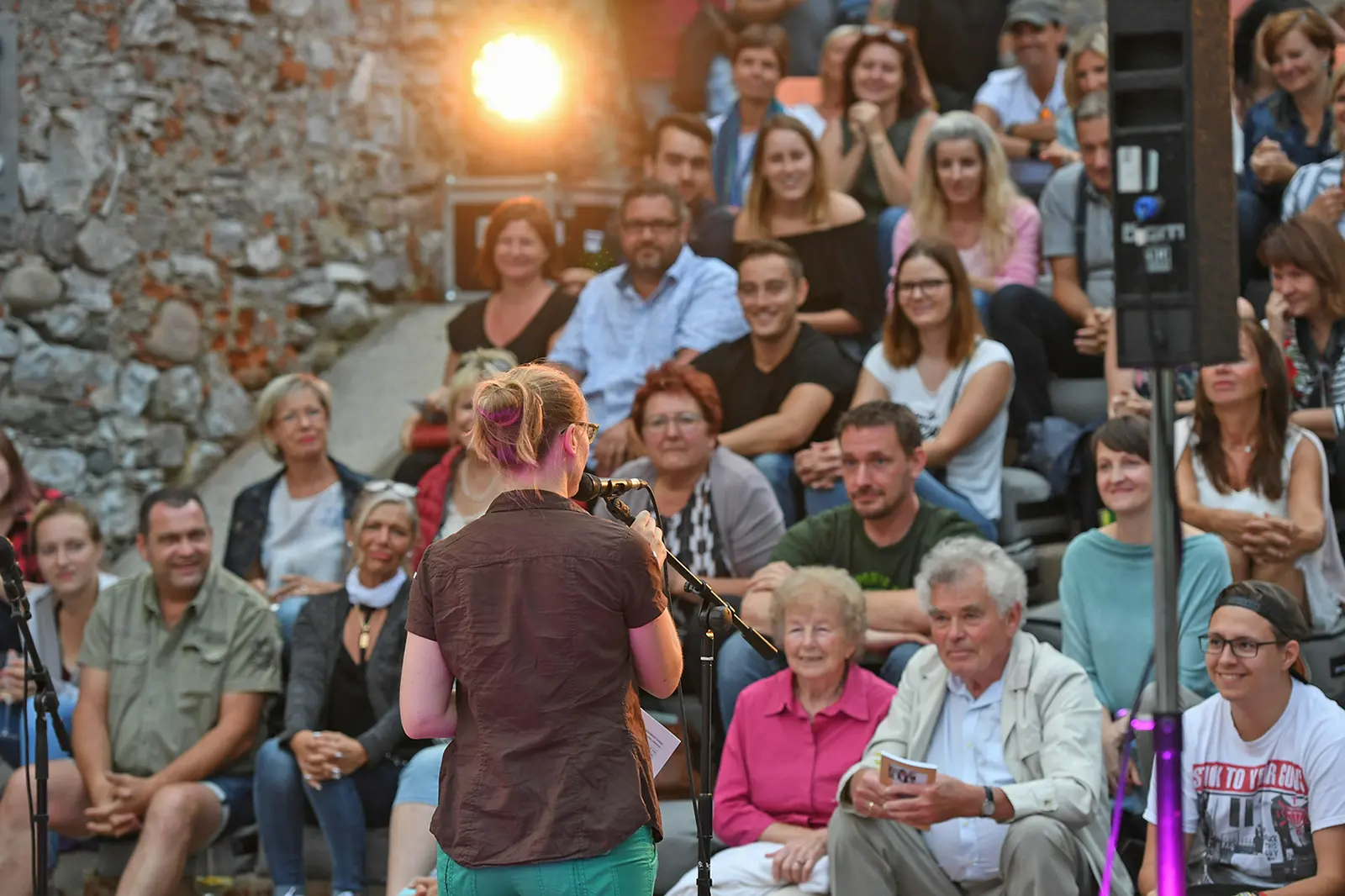 Eine junge Frau spricht im Freien vor Zuschauern in ein Mikrofon